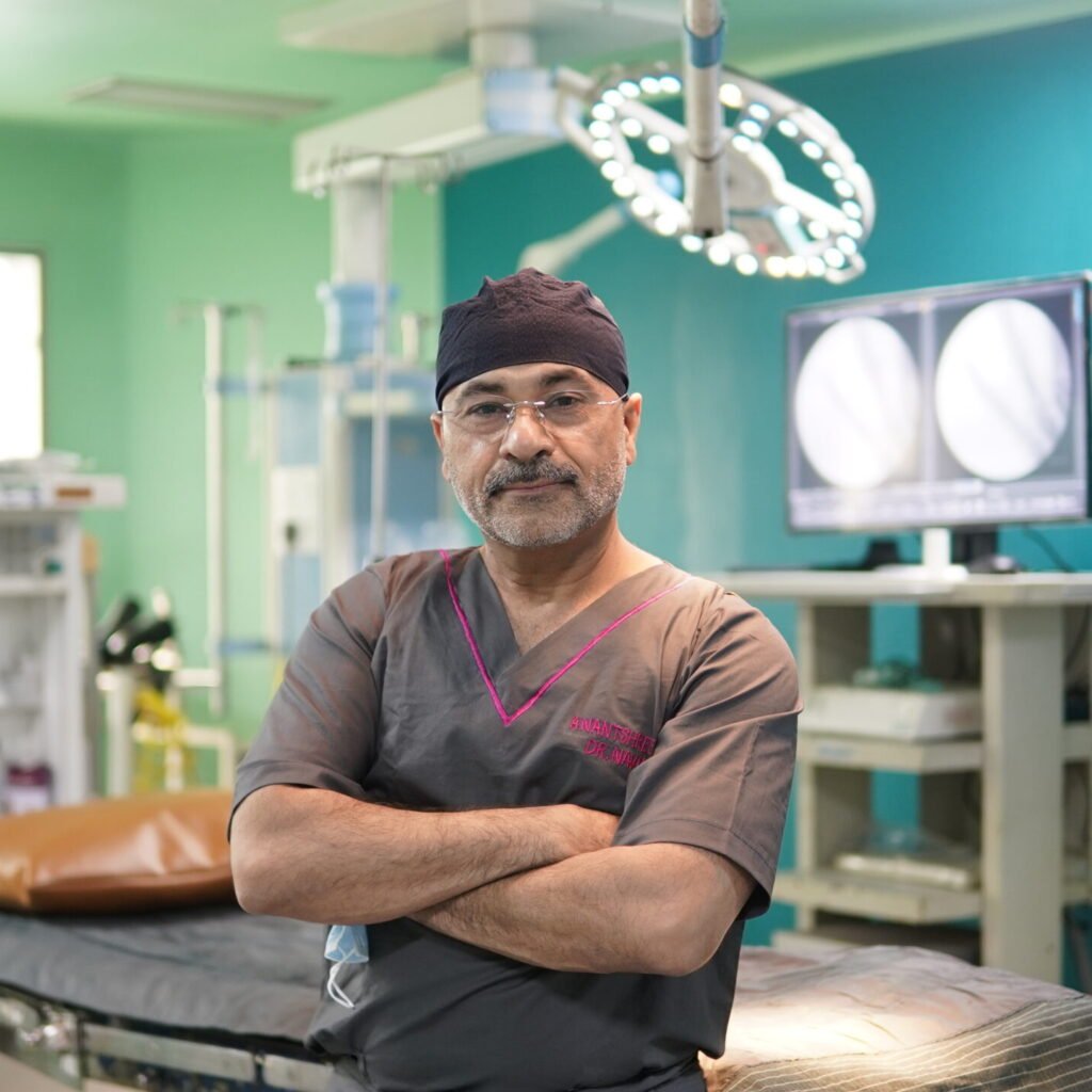 Dr. Navin Batra, orthopaedic surgeon, standing in an operating room at Anantshree Hospital with surgical equipment and medical imaging in the background.