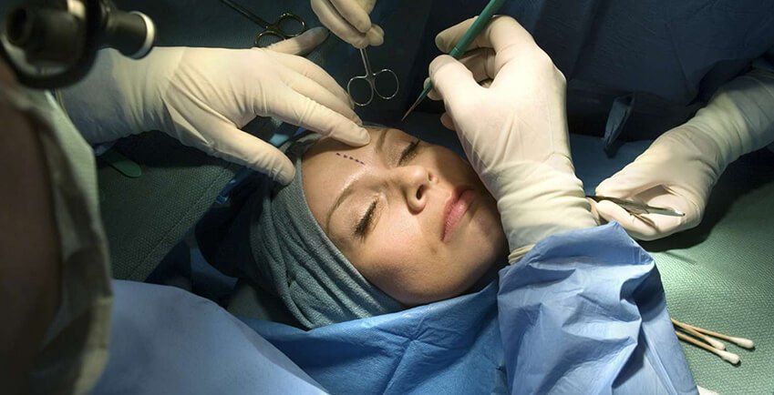 Plastic surgeons performing a facial cosmetic surgery procedure on a female patient in an operating room.