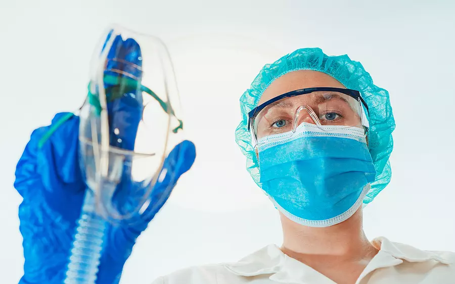 Healthcare professional holding an oxygen mask while wearing protective surgical equipment in a clinical setting.