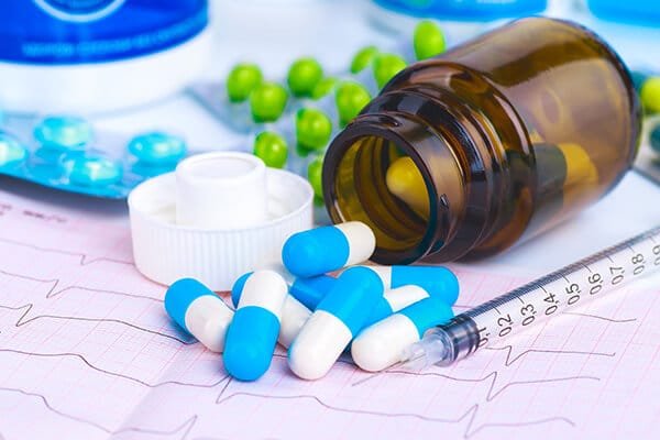 Medicines and capsules beside a medical syringe and prescription chart, representing medication and healthcare treatment.
