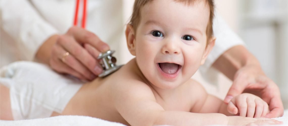 Smiling baby receiving a routine pediatric examination with a doctor using a stethoscope.